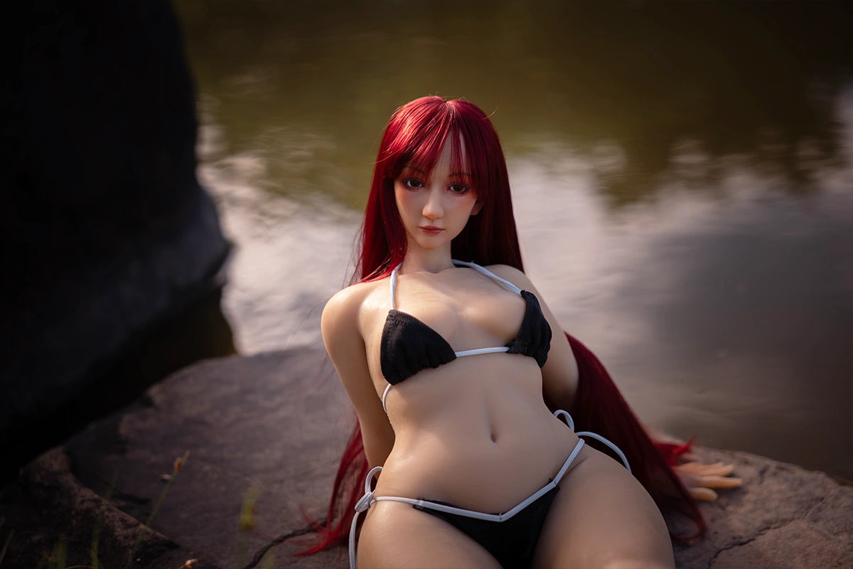 Image of The red-haired Puffypink barbie sex doll wearing a black bikini, sitting on a rock in an outdoor setting.